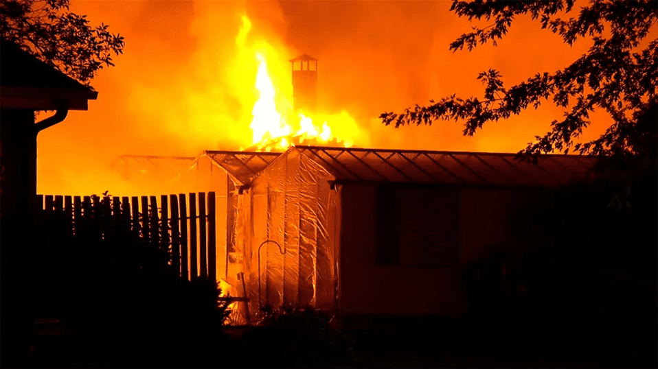 Flames emerge from the greenhouse as firefighters arrive.